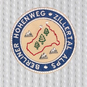 May include: Embroidered patch with a circular design. The patch features text that reads "Berliner Hohenweg Zillertal Alps". The center has a map with trees and mountains in green, red, and gray, set on a tan background.
