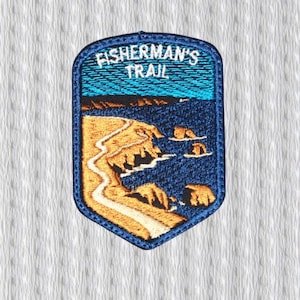 May include: Embroidered patch with a coastal landscape design. The patch features a blue border and the text "FISHERMAN'S TRAIL" at the top. The scene depicts a winding path along a tan cliffside, with blue water and small islands.