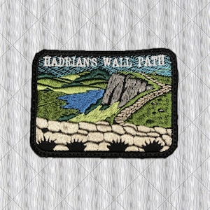 Puede incluir: Parche bordado con la inscripción "Hadrian's Wall Path", que representa un paisaje con un lago azul, colinas verdes, un sendero de piedra y un acantilado rocoso. El parche tiene un borde negro.