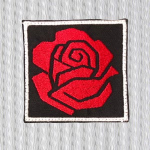 Può includere: Toppa quadrata ricamata con una rosa rossa su sfondo nero. La rosa è delineata in nero e presenta un design dettagliato. La toppa ha un bordo bianco ed è per abbigliamento o accessori.