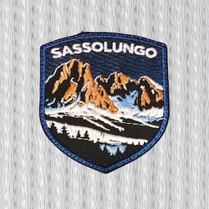 May include: Embroidered patch with the text "SASSOLUNGO" above a mountain range. The patch is shield-shaped with a navy blue border and background. The mountains are brown and white, with a snowy base and a dark blue sky.