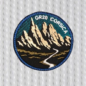 Può includere: Toppa ricamata circolare raffigurante una catena montuosa e un fiume. La toppa ha un bordo blu e la scritta "GR20 CORSICA" in bianco. Le montagne sono beige e nere, su sfondo turchese.