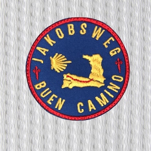 Op de afbeelding: Ronde patch met de gele woorden "JAKOBS WEG BUEN CAMINO" op een blauwe achtergrond. Het heeft een gele sint-jakobsschelp, een kaartomtrek en rode kruisen. De rand is rood.