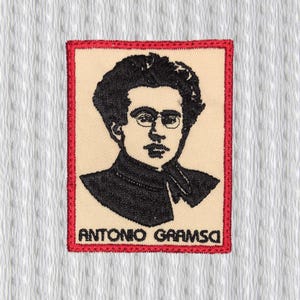 Könnte beinhalten: Gestickter Aufnäher mit einem Schwarz-Weiß-Porträt eines Mannes mit Brille und dem Text "ANTONIO GRAMSCI" in Schwarz. Das Porträt befindet sich auf beigem Hintergrund, umrahmt von einem roten Rand. Der Aufnäher ist für Kleidung oder Accessoires bestimmt.