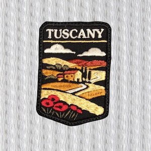 Könnte beinhalten: Gestickter Aufnäher mit dem Wort "TUSCANY" oben. Der Aufnäher zeigt eine Landschaftsszene mit sanften Hügeln, einem Bauernhaus, einer kurvenreichen Straße und roten Mohnblumen. Der Aufnäher hat einen schwarzen Rand.