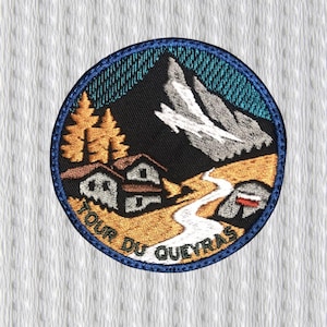 Op de afbeelding: Geborduurde patch met een cirkelvormig ontwerp met een berglandschap. De patch bevat een bergtop, een rivier, bomen en twee huizen. De tekst "TOUR DU QUEYRAS" is langs de onderrand gebogen, met een blauwe rand.