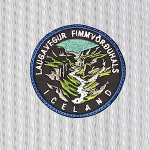 Peut inclure: Écusson brodé circulaire avec un paysage de montagne et le texte "LAUGAVEGUR FIMMVÖRÐUHALS ICELAND". Le patch a un fond noir avec des accents verts, blancs et bleus, et une bordure bleue. Le patch est sur un fond blanc texturé.