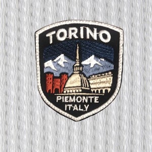May include: Embroidered patch featuring the city name "TORINO" at the top. The patch depicts a cityscape with a domed building, mountains, and the text "PIEMONTE ITALY" at the bottom. The patch has a black border.