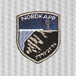 Puede incluir: Parche bordado con la palabra "NORDKAPP" en la parte superior. El parche presenta un paisaje con un cielo azul oscuro, un mar azul claro y un acantilado negro. Las coordenadas 71°10'21"N están en la parte inferior.
