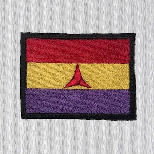Könnte beinhalten: Gestickter Aufnäher mit rechteckigem Design in Rot, Gold und Lila. Ein stilisiertes rotes Symbol ist auf dem goldenen Abschnitt zentriert. Der Aufnäher hat einen schwarzen Rand und ist vor einem weißen, strukturierten Hintergrund platziert.