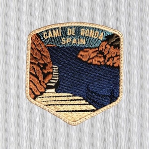 Pode incluir: Patch bordado com uma paisagem costeira e o texto "CAMI DE RONDA SPAIN". O design inclui um mar azul, falésias castanhas e uma borda bege. O patch é adequado para uma jaqueta ou bolsa.