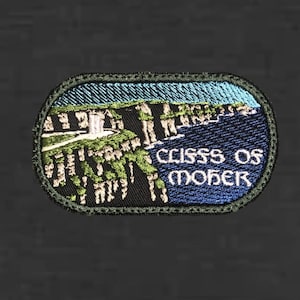 May include: Embroidered patch featuring a coastal landscape with cliffs, ocean, and sky. The patch has a dark green border and includes the text "Cliffs of Moher" in white lettering. The design incorporates shades of blue, green, and white.