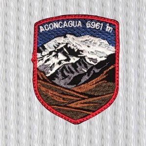 May include: Embroidered patch featuring a mountain landscape with the text "ACONCAGUA 6961 ft" in white. The patch has a red border and depicts a snow-capped mountain range against a blue sky. The lower portion shows brown and gray terrain.