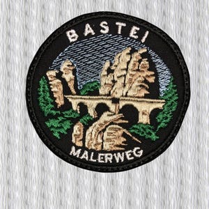 May include: Circular embroidered patch with a black border. The patch features the text "BASTEI" above a bridge and rock formation, with "MALERWEG" below. The design incorporates green, tan, and blue colours.