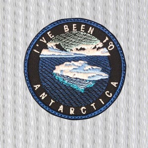 May include: Embroidered patch with a circular design featuring a blue and white Antarctic landscape. The text "I'VE BEEN TO ANTARCTICA" is embroidered around the edge in white letters. The patch has a black border and is set against a white textured background.