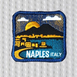 Può includere: Toppa ricamata raffigurante un paesaggio di Napoli, Italia, con un tramonto sulle montagne e lo skyline della città. La toppa ha un bordo blu, con la scritta "NAPLES ITALY" in bianco.