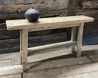 May include: A rustic wooden console table with a single shelf. The table is made of reclaimed wood and has a natural, weathered finish. A black ceramic vase sits on the top of the table.