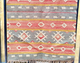 May include: A colourful woven rug with a geometric pattern in shades of red, yellow, grey, and white. The rug has a fringe border.