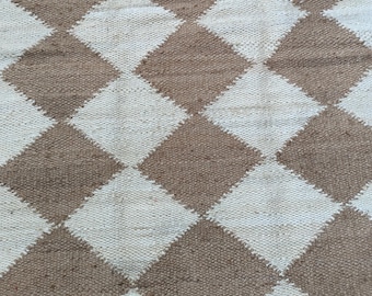 May include: A woven rug featuring a repeating diamond design. The diamonds alternate between a light beige and a medium brown hue. The rug has a textured appearance, possibly made from natural fibres.