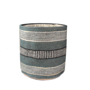 May include: A woven storage basket with a blue, white and black striped pattern. The basket is made of natural fibres and has a round shape.