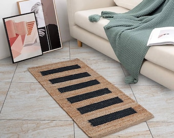 May include: A rectangular jute rug with six black stripes. The rug is placed on a tiled floor, with a cream-colored sofa and framed artwork in the background. The rug's natural tones and geometric design add a touch of rustic charm to the space.