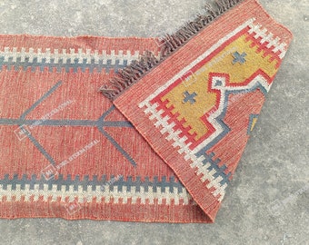 Puede incluir: Una alfombra roja, amarilla y azul con estampado y flecos en los bordes. La alfombra está doblada por la mitad, mostrando ambos lados del estampado.