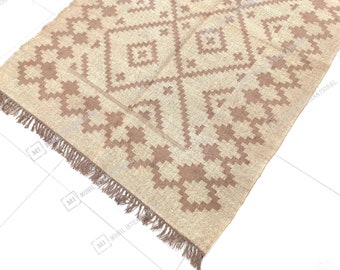 May include: A beige and brown patterned rug with a fringe border. The rug has a geometric design with a diamond pattern.
