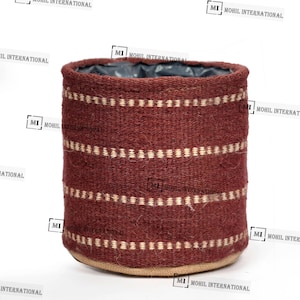 Puede incluir: Una cesta cilíndrica tejida, de color burdeos, con bandas horizontales de líneas punteadas blancas. La cesta tiene una base de fibra natural y un forro interior oscuro. Para la decoración del hogar.
