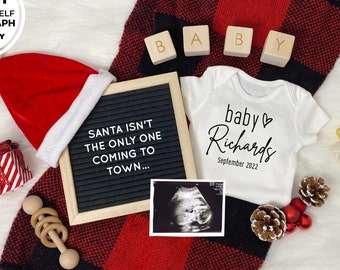 May include: A festive pregnancy announcement featuring a Santa hat, baby onesie, ultrasound image, and wooden blocks spelling "BABY." The onesie reads "baby Richards September 2022." A letter board says "SANTA ISN'T THE ONLY ONE COMING TO TOWN..."