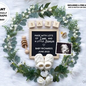 May include: A white background with a wreath of greenery and white flowers. In the center of the wreath is a black letter board with the text "MADE WITH LOTS OF Love AND A LITTLE Science" and "BABY RICHARDS JUNE 2022". There are also wooden blocks that spell out "BABY", a pacifier, a wooden rattle, and a baby ultrasound image.