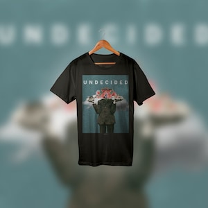 May include: Black t-shirt with a graphic print of a person with a head full of flowers holding two trays. The text "UNDECIDED" is printed on the shirt.