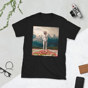May include: Black t-shirt featuring a graphic print of a person with a tiger head standing in a field of pink flowers. The graphic has a vintage, surrealist aesthetic.