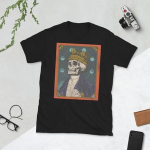 May include: Black t-shirt with a graphic print of a skull wearing a crown and surrounded by a circle of moons. The graphic is set against a red background with a gold border.