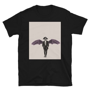 May include: A black t-shirt with a graphic of a person with wings. The person is wearing a suit and has a hat on. The background is a light beige color.