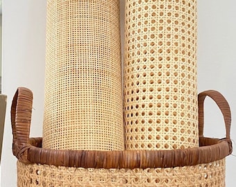 May include: Two rolls of natural cane webbing in a woven wicker basket with brown handles. The webbing is used for chair seats and backs.