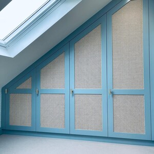 Puede incluir: Un conjunto de cuatro puertas de armario azules con paneles de ca&ntilde;a blanca tejidos. Las puertas est&aacute;n inclinadas para adaptarse a un techo inclinado.