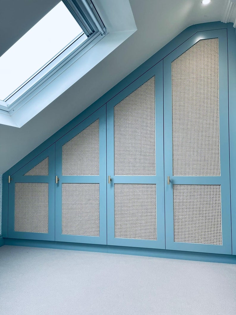 Puede incluir: Un conjunto de cuatro puertas de armario azules con paneles de ca&ntilde;a blanca tejidos. Las puertas est&aacute;n inclinadas para adaptarse a un techo inclinado.