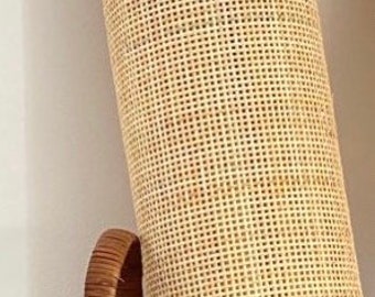 May include: A rolled-up, light brown woven cane material, possibly for furniture or decor, rests inside a woven basket. The cane has a grid-like pattern, and the basket has a curved handle.