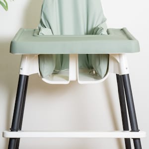 May include: A white and green high chair with black legs. The chair has a removable tray and a padded seat.