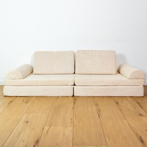 May include: A cream-coloured corduroy sofa with two armrests and a modular design. The sofa is sitting on a light wood floor.