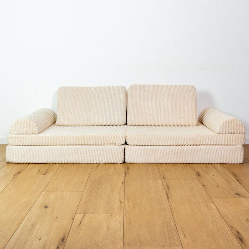 May include: A cream-coloured corduroy sofa with two armrests and a modular design. The sofa is sitting on a light wood floor.