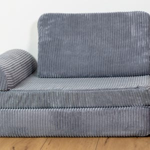 May include: A grey corduroy sofa with a thick, padded back and armrests. The sofa is made of a soft, comfortable fabric and has a simple, modern design.