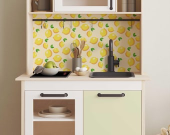 Può includere: Un set da gioco per cucina in legno bianco con un piano cottura, un lavandino e ante degli armadietti neri. Il paraschizzi presenta un motivo a limone.