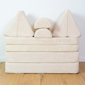 May include: A set of beige corduroy cushions in various shapes, including triangles and half-circles, stacked on top of each other to form a small sofa-like structure.