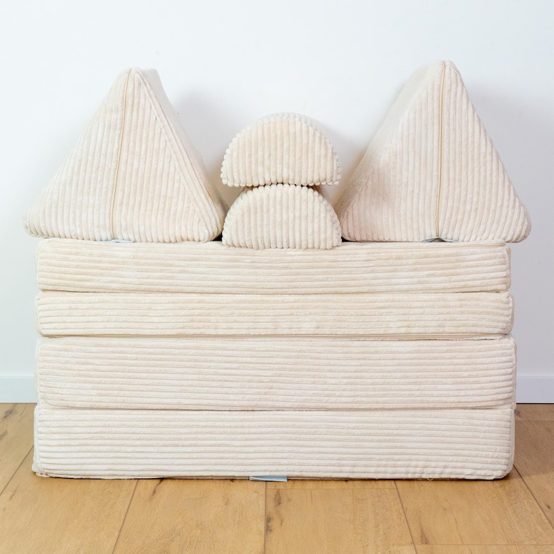 May include: A set of beige corduroy cushions in various shapes, including triangles and half-circles, stacked on top of each other to form a small sofa-like structure.