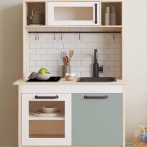 May include: A white and wood play kitchen with a black sink, stovetop, and cabinet handles. The kitchen has a white tiled backsplash and a shelf with hooks for hanging utensils.