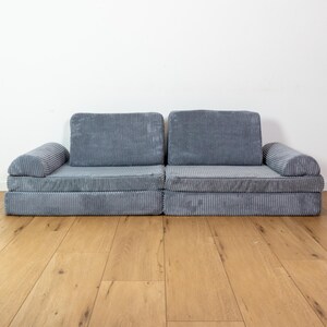 May include: A grey corduroy sectional sofa with a modular design. The sofa has a low profile and is made of a soft, comfortable fabric.