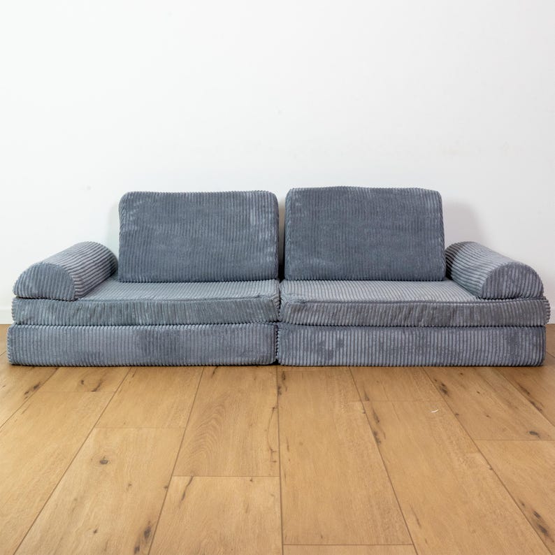 May include: A grey corduroy sectional sofa with a modular design. The sofa has a low profile and is made of a soft, comfortable fabric.