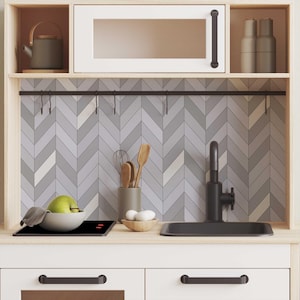 May include: A white play kitchen with a black stovetop, a black sink, and a gray and white chevron tiled backsplash. The kitchen has a black metal rack with hooks above the backsplash.