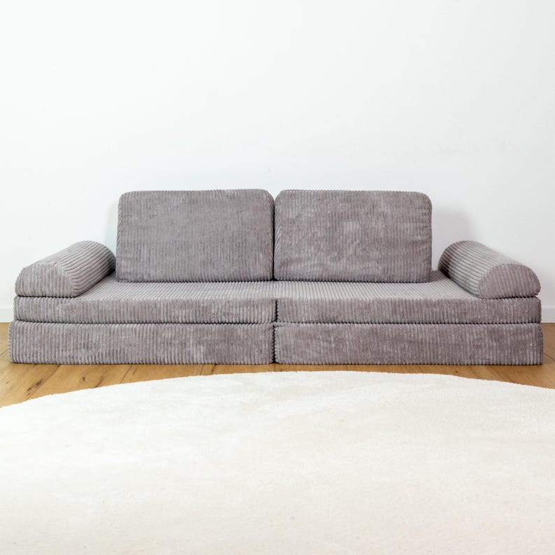 May include: A grey corduroy sofa with a modular design. The sofa has a thick, padded seat and back cushions. The sofa is in a modern style and would be a great addition to any living room.